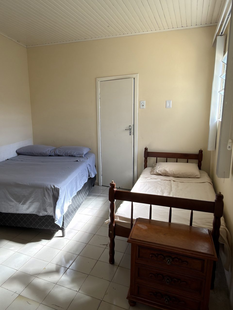 O quarto do Quarto 2: a cama de casal e a de solteiro, de madeira, com a janela ao lado.